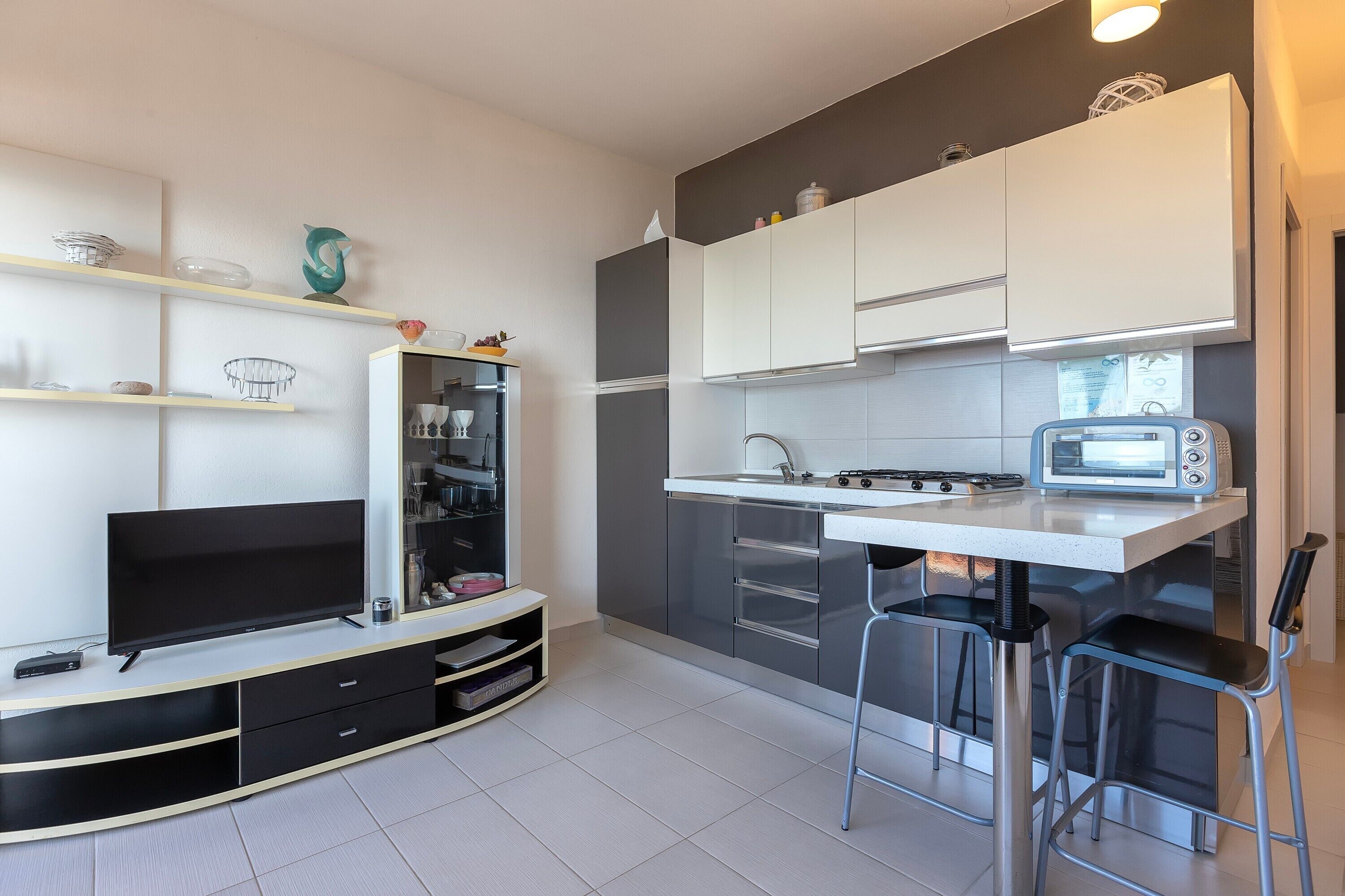 A modern kitchen with a flat-screen TV, a microwave, and a small dining area with two bar stools.