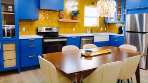 A modern kitchen with blue cabinets, a wooden dining table, and a stainless steel refrigerator.