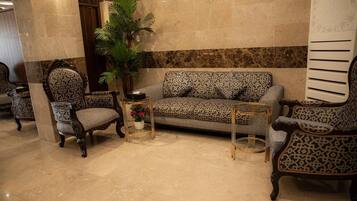 A lobby with a patterned sofa, matching armchairs, a small table with a plant, and a decorative mirror.