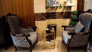 A lobby with two patterned armchairs, a small table with a vase of flowers, and a trash bin.