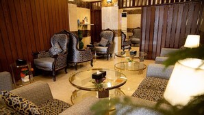 A lobby with patterned armchairs, a glass coffee table, and a sofa with a leopard print cushion.