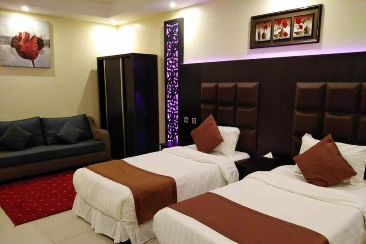 Una habitación de hotel con dos camas individuales, un sofá, un armario y un panel decorativo en la pared.