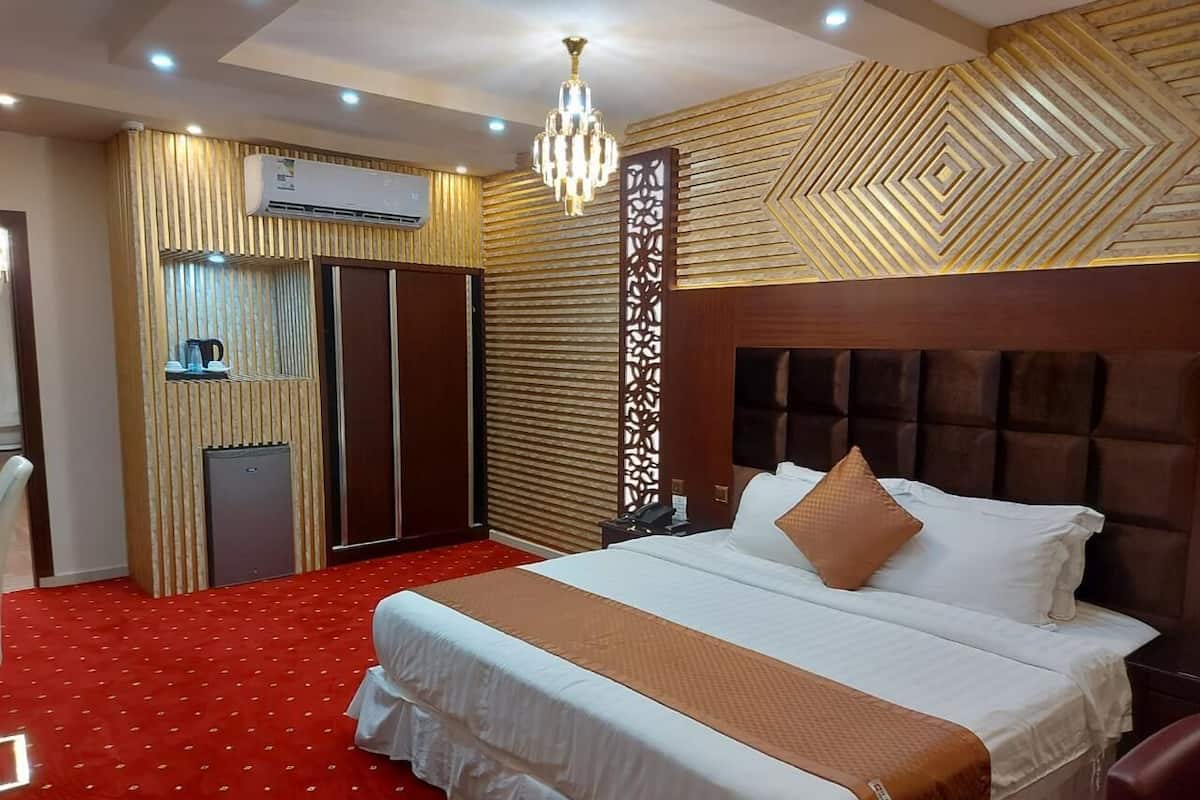 Una habitación de hotel con una cama grande, alfombra roja, cabecera de madera, candelabro, armario y un panel decorativo.