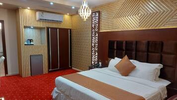 A hotel room with a large bed, a red carpet, a wooden headboard, a chandelier, a wardrobe, and a decorative panel.