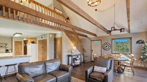 A spacious living area with a high ceiling, wooden beams, a staircase, a dining area, and a kitchen. - Peaceful Cabin with Epic Mountain Views! (Florissant)