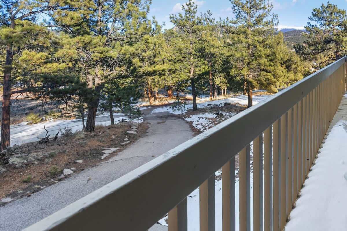 A snowy landscape with a paved path, trees, and a metal railing.