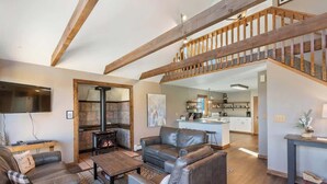 A spacious living area with a fireplace, leather sofas, a wooden staircase, and a kitchen in the background. - Peaceful Cabin with Epic Mountain Views! (Florissant)