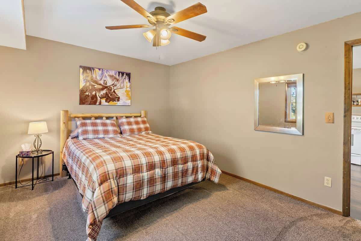 A bedroom with a bed, a ceiling fan, a nightstand, a lamp, a painting, and a mirror.