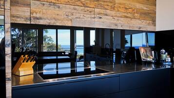 A modern kitchen with a large window, a wooden ceiling, and a view of the sea.