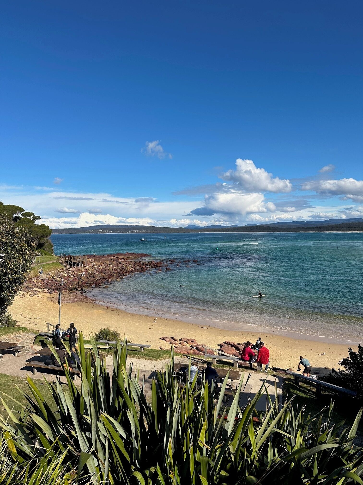 A beach with clear blue water, a rocky shoreline, and a wooden walkway.
