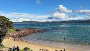 A beach with clear blue water, a rocky shoreline, and a wooden walkway.