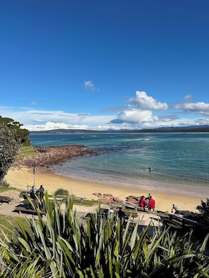 Une plage à l’eau d’un bleu cristallin, avec une côte rocheuse et une promenade en bois.
