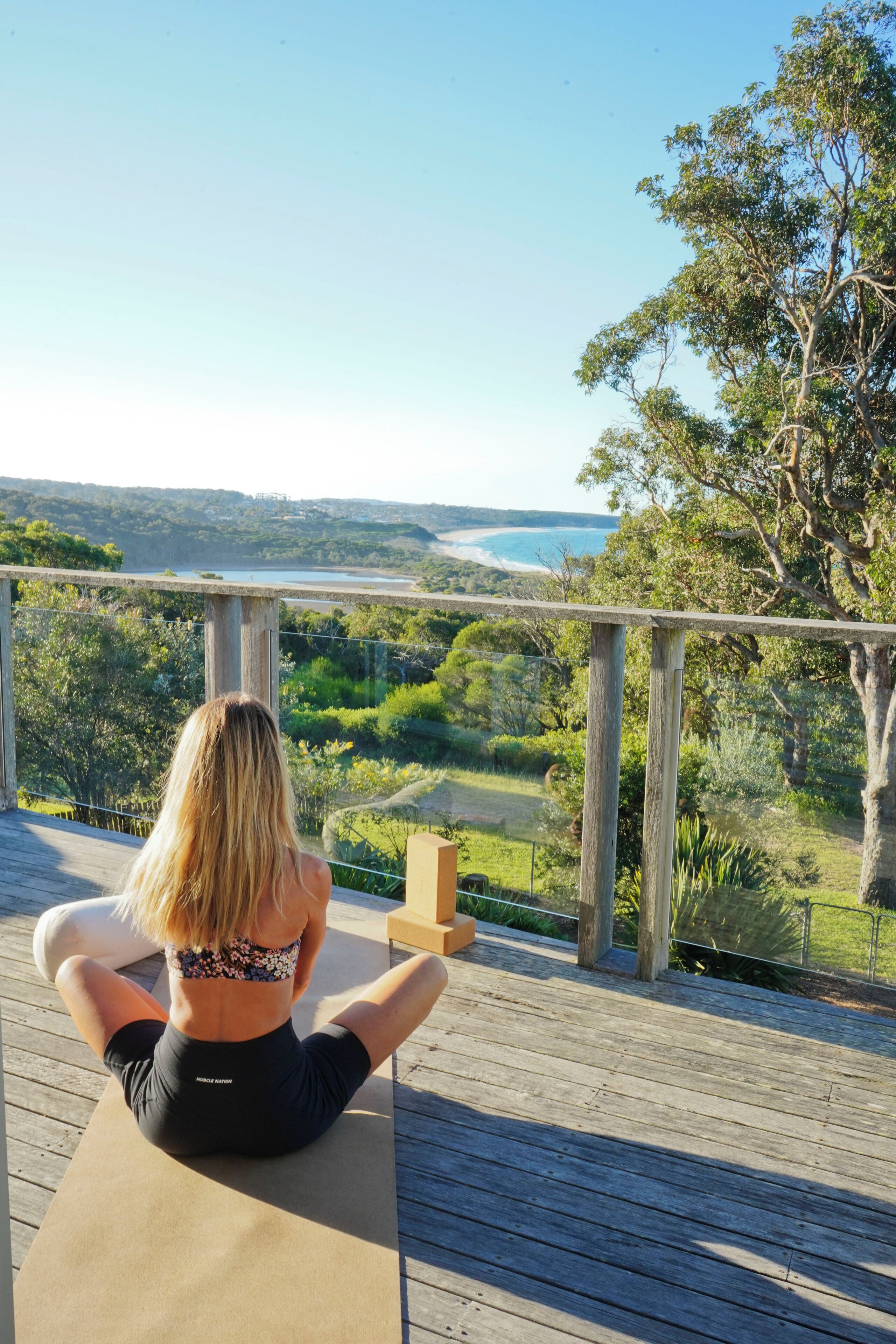 A person sitting on a wooden deck with a view of a landscape including trees and a body of water.
