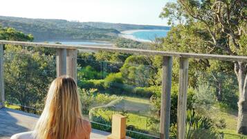 A person sitting on a wooden deck with a view of a landscape including trees and a body of water.