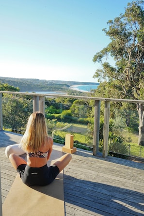 Une personne est assise sur une terrasse en bois, d’où l’on peut admirer un paysage comprenant des arbres et une étendue d’eau.