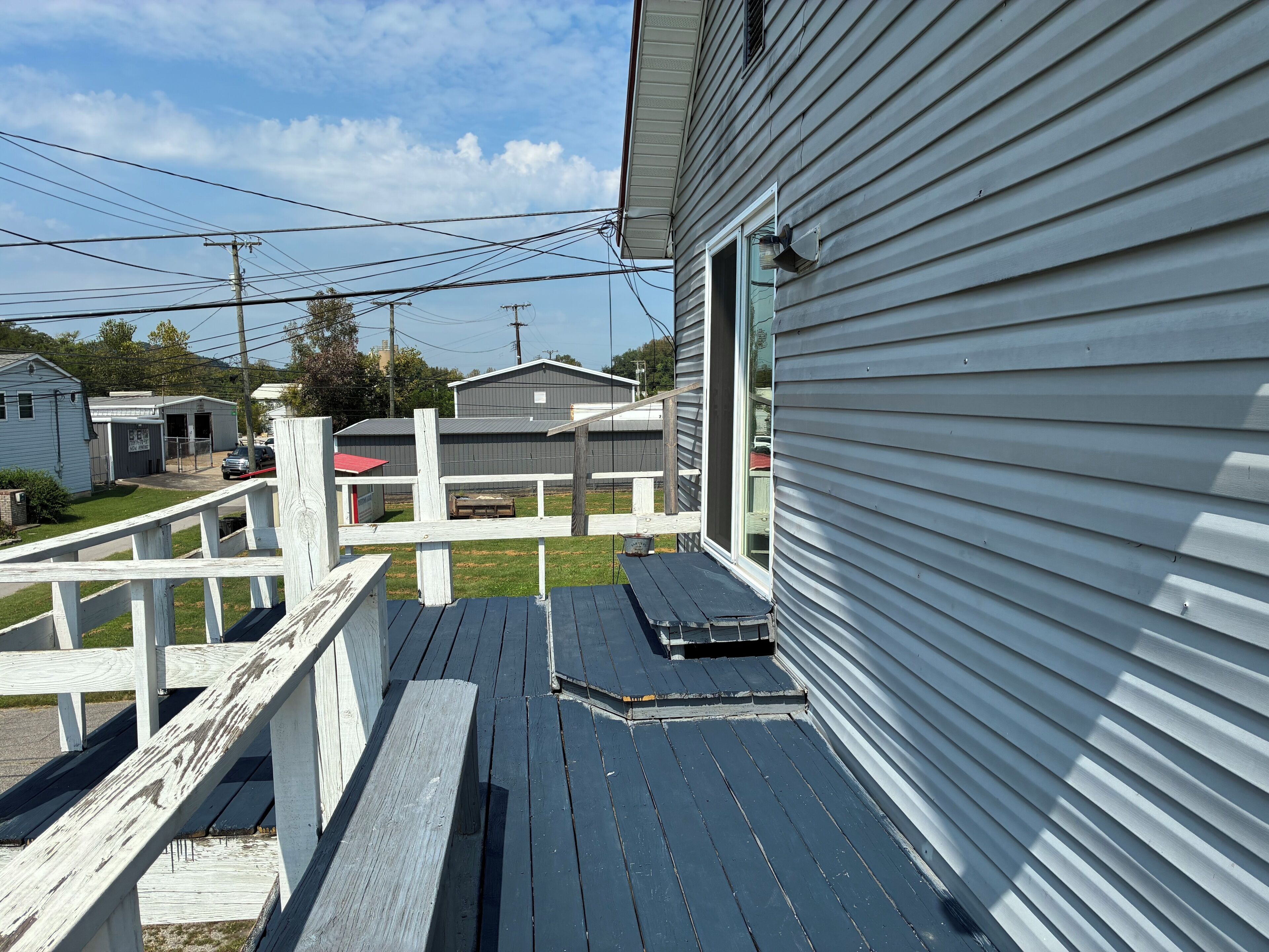A wooden deck with a bench, a white fence, and a house with a grey exterior.