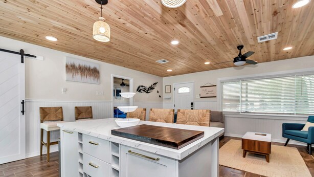 A spacious kitchen with a large island, wooden ceiling, and modern lighting fixtures.