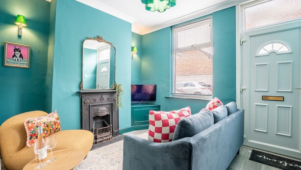 A teal-colored living room with a sofa, a small table with glasses, a fireplace, and a television.