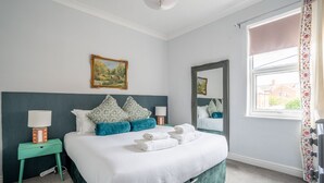 A neatly arranged bedroom with a bed, a bedside table, a mirror, and a window with curtains.