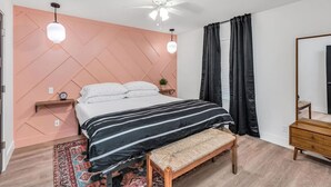 Een slaapkamer met een bed, nachtkastjes, een bankje, een plafondventilator en een grote spiegel.