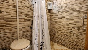 A bathroom with a wooden wall design, a toilet, a shower with a floral curtain, and a wooden door. - Fully equipped cabins, on the jungle route on the way to the Moconá Falls. (El Soberbio)