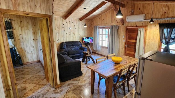 A wooden cabin interior with a living area, dining table, and kitchen. - Fully equipped cabins, on the jungle route on the way to the Moconá Falls. (El Soberbio)