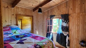 A wooden cabin room with a bed, a window with curtains, and a hanging light fixture. - Fully equipped cabins, on the jungle route on the way to the Moconá Falls. (El Soberbio)