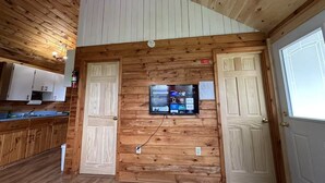 A wooden interior with a kitchen area, two doors, and a mounted TV displaying various channels. - Seabreeze Retreat-Cozy waterfront  3-bedroom, one minute from PEI National Park (York)