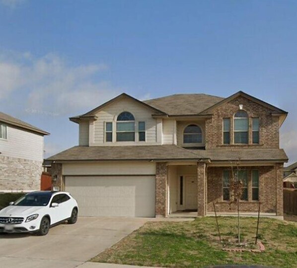 A two-story house with a garage, a driveway, and a parked car. - Contemporary family-friendly 4-bedroom home in Killeen, located near Fort Hood! (Killeen)