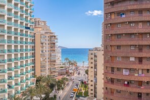 A high-rise building with balconies, a street in the foreground, and a clear view of the sea.