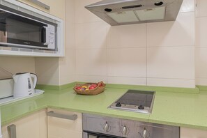 A kitchen with a microwave, kettle, and a basket of fruit on the counter.