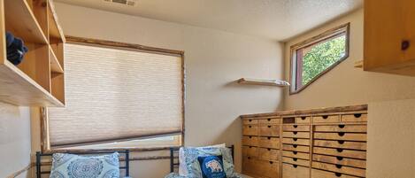 Una habitación compacta con dos camas individuales, un aparador de madera, una ventana con persianas y un tragaluz pequeño.