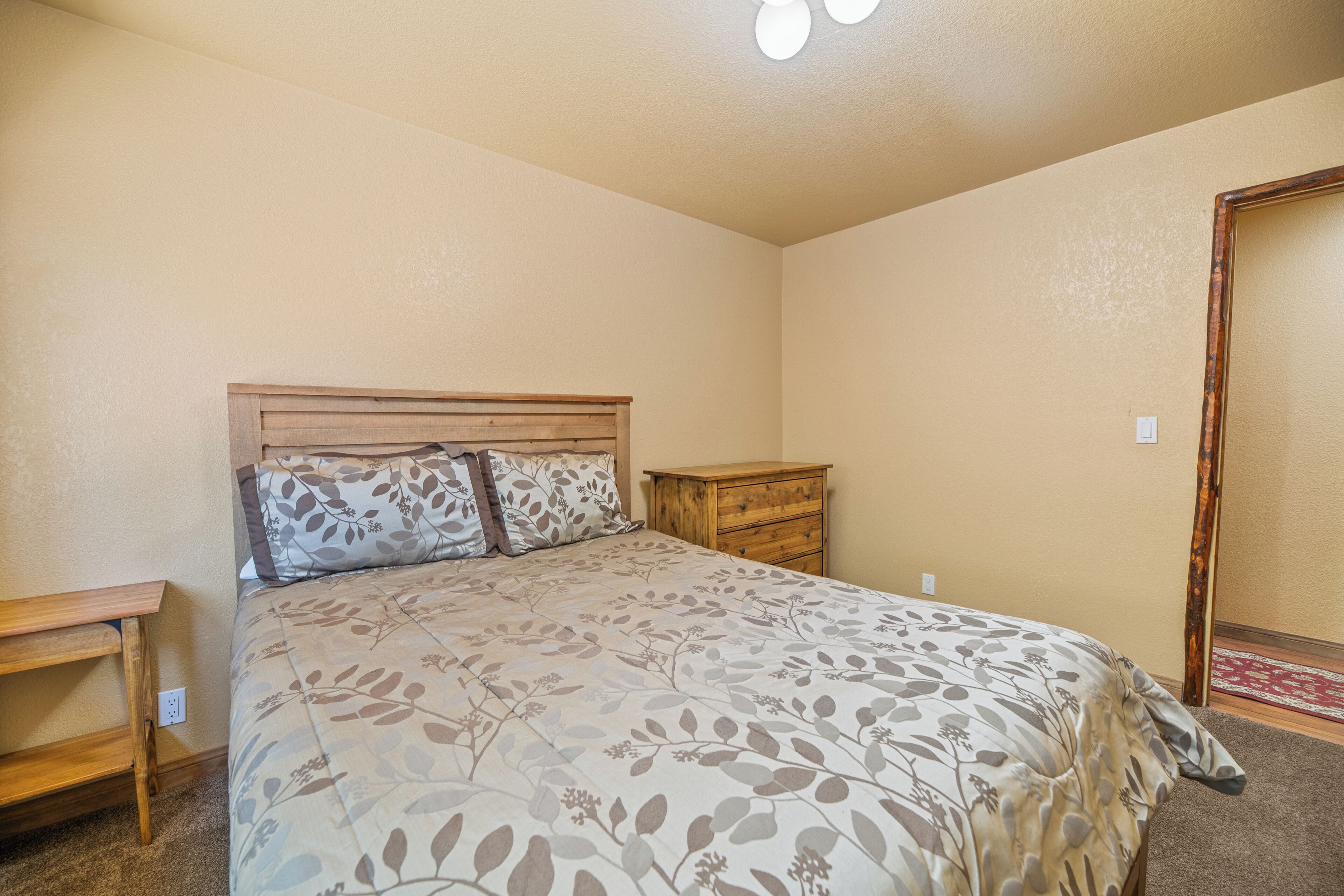 A bedroom with a bed, wooden nightstand, dresser, and a door.