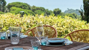 Ein Esstisch mit sauberem Geschirr und Blick auf einen üppigen Garten und das Meer.