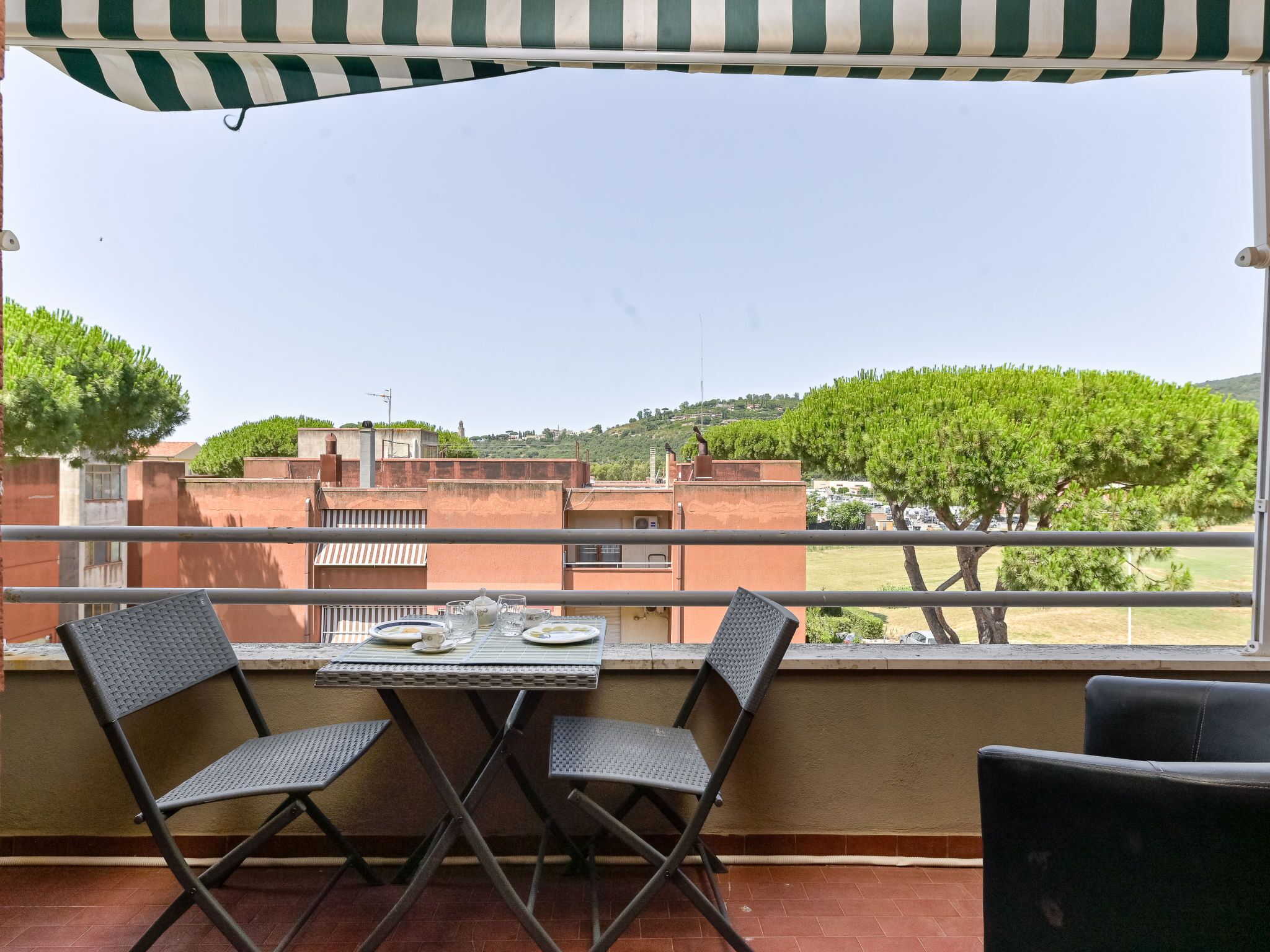 Ein Balkon mit Tisch für zwei Personen, mit Blick auf eine Wohngegend mit Bäumen und Gebäuden.