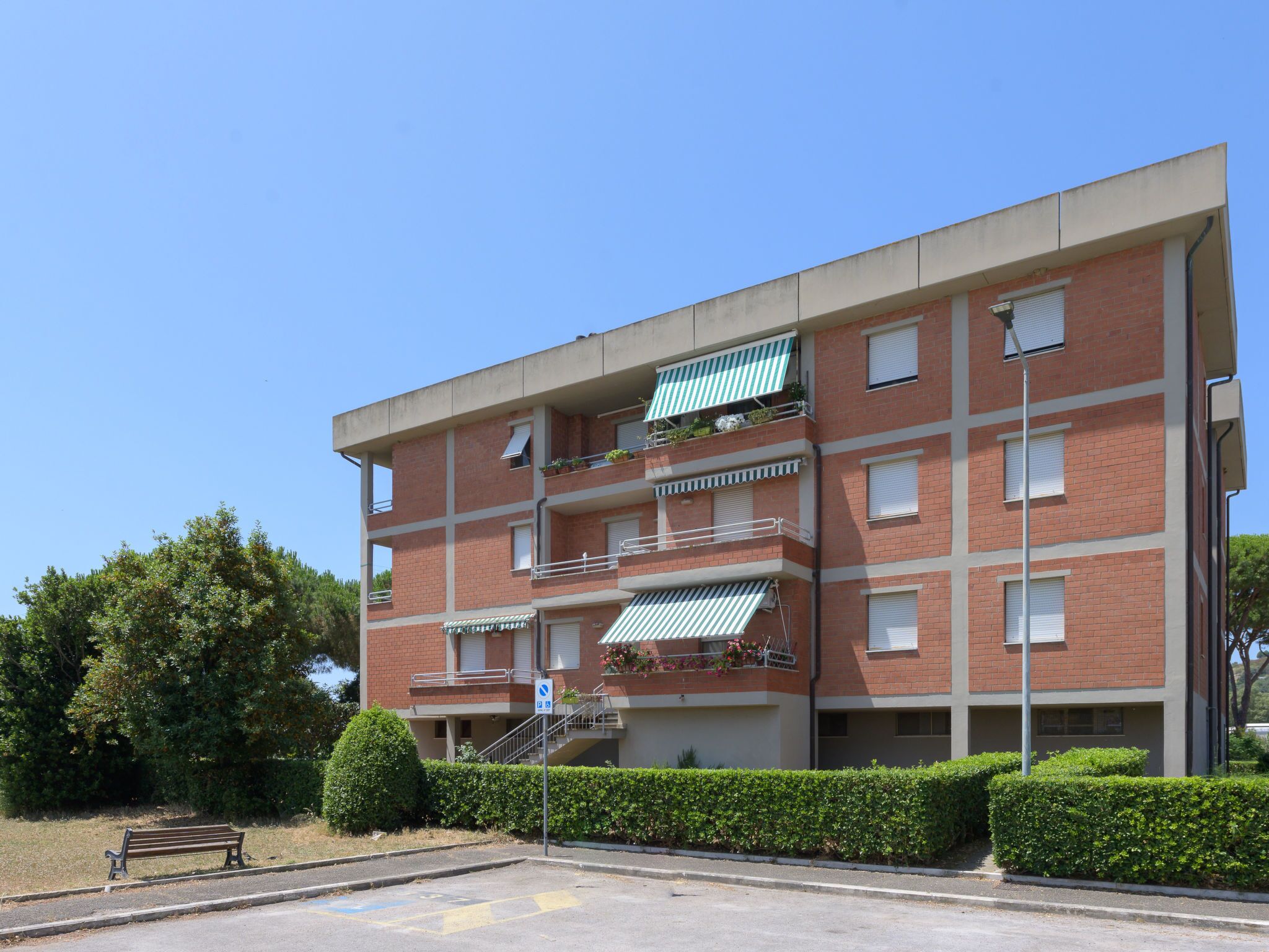 A multi-story brick building with balconies, a parking lot, and a bench.