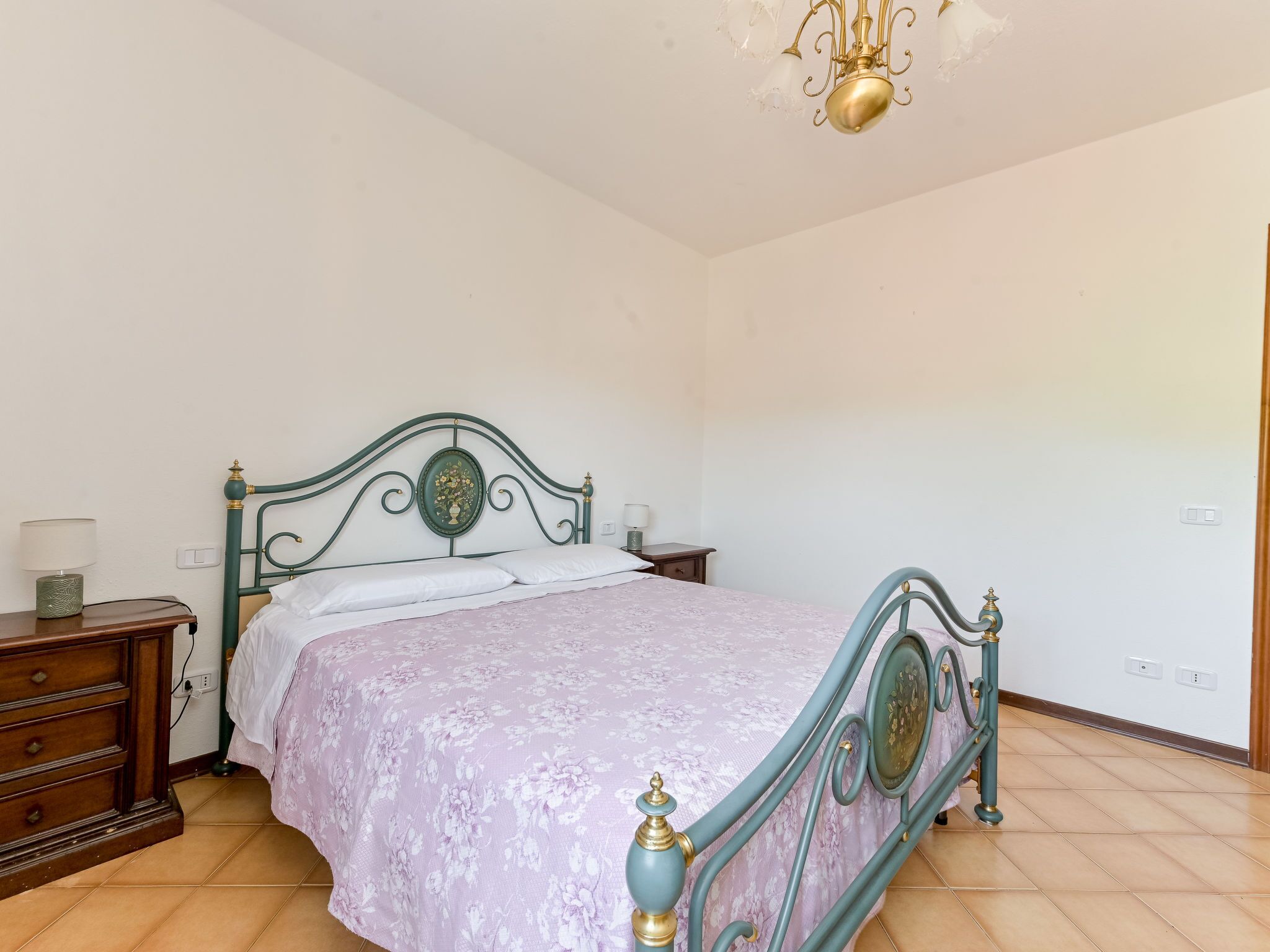 Un dormitorio con cama, cómoda, mesitas de noche y una araña.