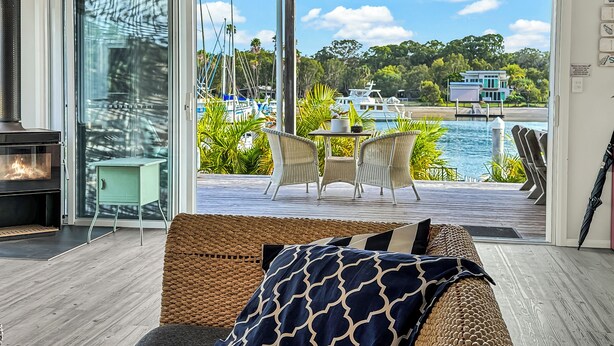 A living room with a glass door leading to a balcony overlooking a marina with boats and a clear sky.