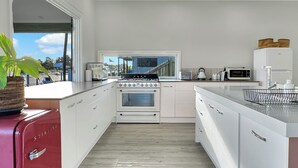 A modern kitchen with white cabinetry, a stainless steel range hood, a red vintage refrigerator, and a large window offering a view of the outdoors.