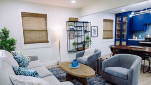 A modern living room with a sofa, armchairs, a coffee table, and a dining area with a kitchen in the background.