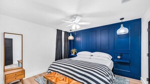 A bedroom with a bed, a wooden nightstand, a bench, a ceiling fan, and a blue wall.