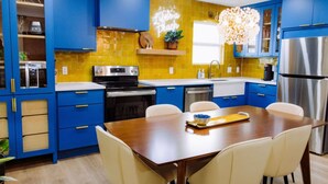 A modern kitchen with blue cabinets, a yellow backsplash, stainless steel appliances, and a wooden dining table with chairs.