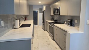 Une cuisine moderne avec des plans de travail blancs, des armoires grises, un réfrigérateur en acier inoxydable, un four à micro-ondes et une cuisinière.