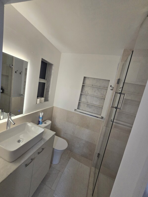 Une salle de bain moderne avec un grand miroir, un lavabo, des toilettes et un espace douche.