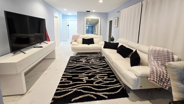 Un salon moderne avec un téléviseur à écran plat, des canapés blancs et un tapis aux motifs noir et blanc.