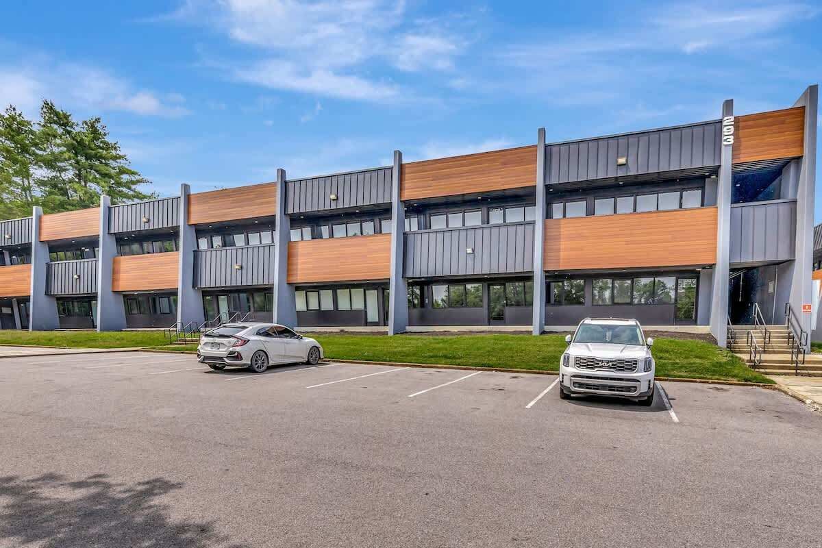 A modern building with a parking lot, two cars, and a clear sky.