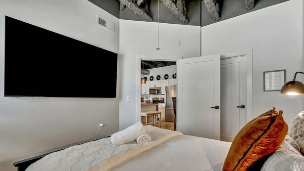 Habitación de hotel moderna con una cama grande, un televisor de pantalla plana y una kitchenette al fondo.