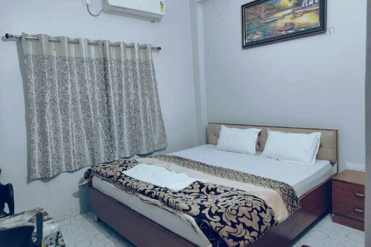 A bedroom with a bed, curtains, a painting, and a bedside table.