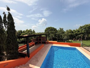 Una piscina amb terrassa de pedra, zona de barbacoa i una pèrgola.
