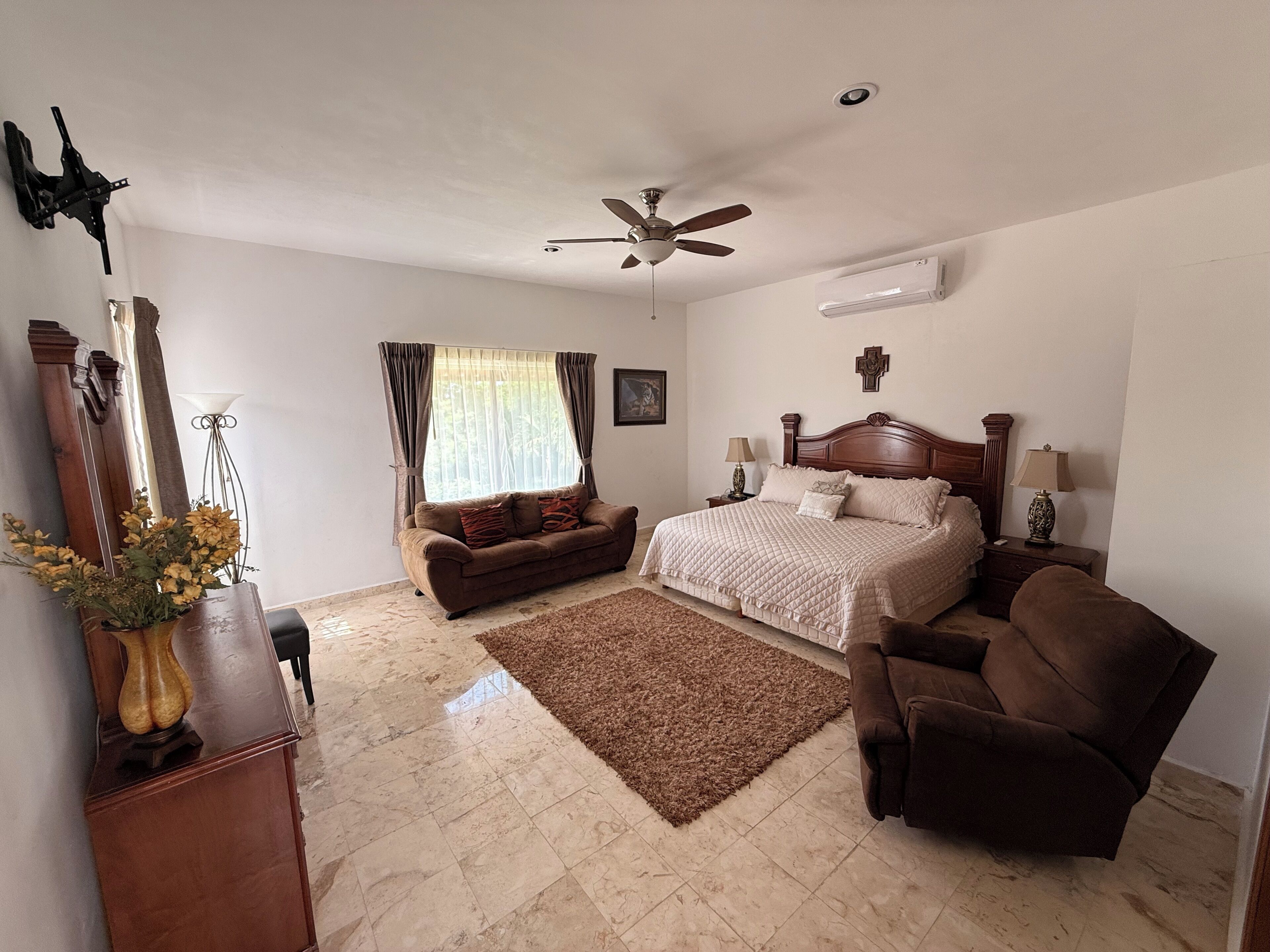 Une chambre à coucher comprenant un lit, une chaise, un canapé, un ventilateur de plafond et un appareil de climatisation.